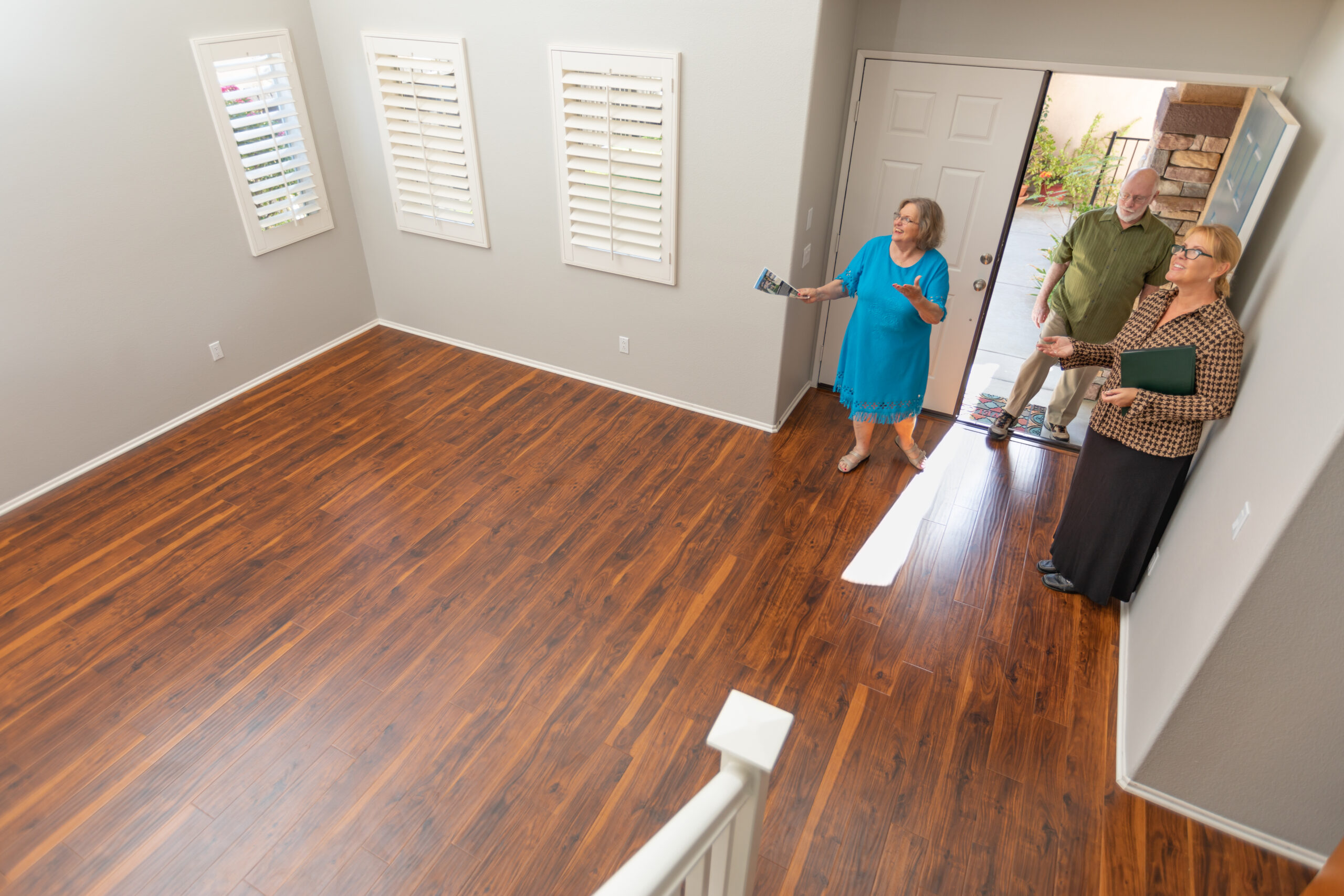 Female Real Estate Agent Showing Senior Adult Couple A New Home.
